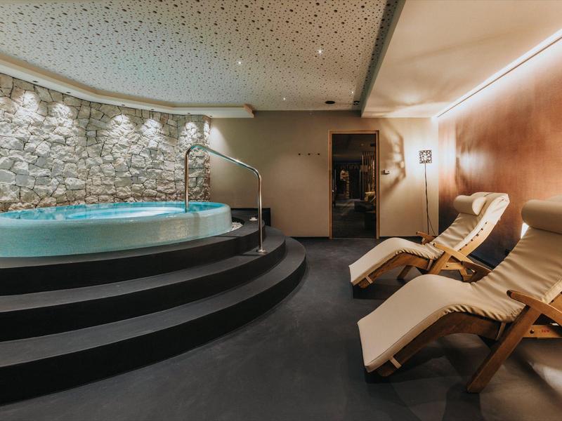 Moderne Wellnessoase mit Rundbecken auf schwarzen Stufen und vier hellen Holzliegen.