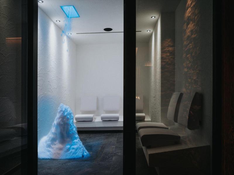 Moderner Raum mit weißen Wänden, Sitzbänken, und leuchtender blauer Eiskulptur in der Mitte.