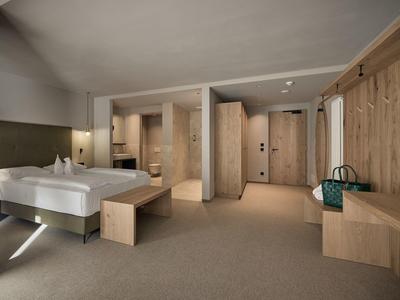 Modernes Hotelzimmer mit großem Bett, Holzmöbeln und Teppichboden in neutralen Farben.