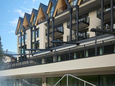 Moderner Hotelbau mit zackigem Dach, Balkonreihen und Holzterrasse am Wasserrand.