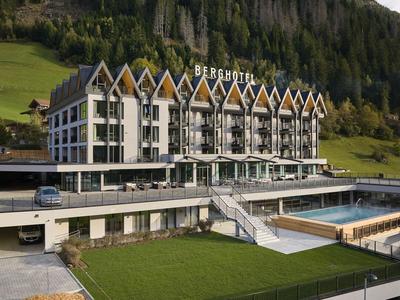 Modernes Hotel mit spitzen Giebeln, großer Glasfront und grüner Berglandschaft im Hintergrund.