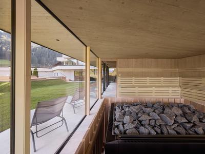 Moderne Holzsauna mit Sicht auf einen Garten und Berge.