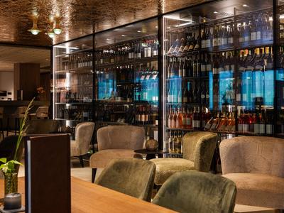 Moderner Hotelbarbereich mit gemütlichen Sesseln und beleuchtetem Weinregal aus Glas.