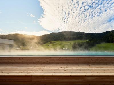 Dampender Außenpool mit Holzdeck vor bewaldeten Hügeln bei Sonnenuntergang.