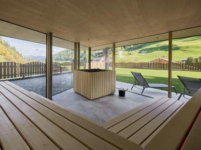Überdachte Terrasse mit Holzbank und zwei Liegestühlen mit Blick auf grüne Hügel.