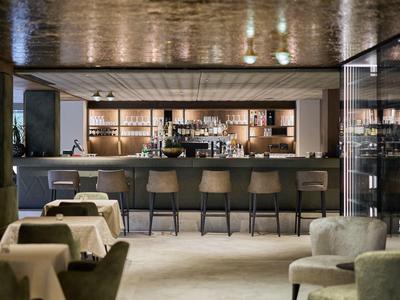Moderner Hotelbarbereich mit Theke, Barhockern und Tischen in elegantem Ambiente.
