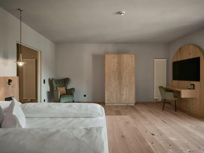 Helles Hotelzimmer mit zwei Einzelbetten, Holzschrank, TV und Schreibtisch auf Holzboden.