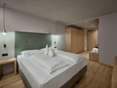 Modernes Hotelzimmer mit Doppelbett, grüner Polsterkopfleiste und Holzmöbeln.