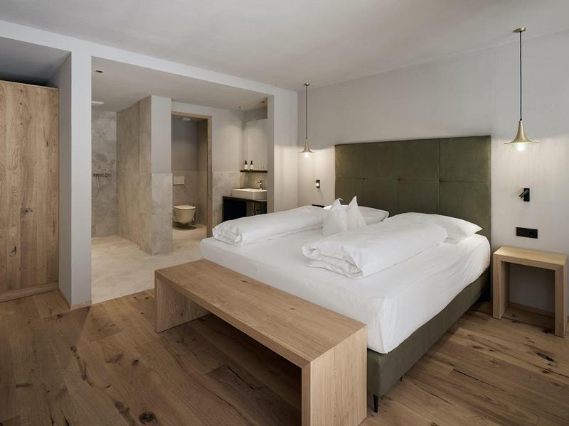 Modernes Hotelzimmer mit Doppelbett, Holzboden und offenem Badbereich.