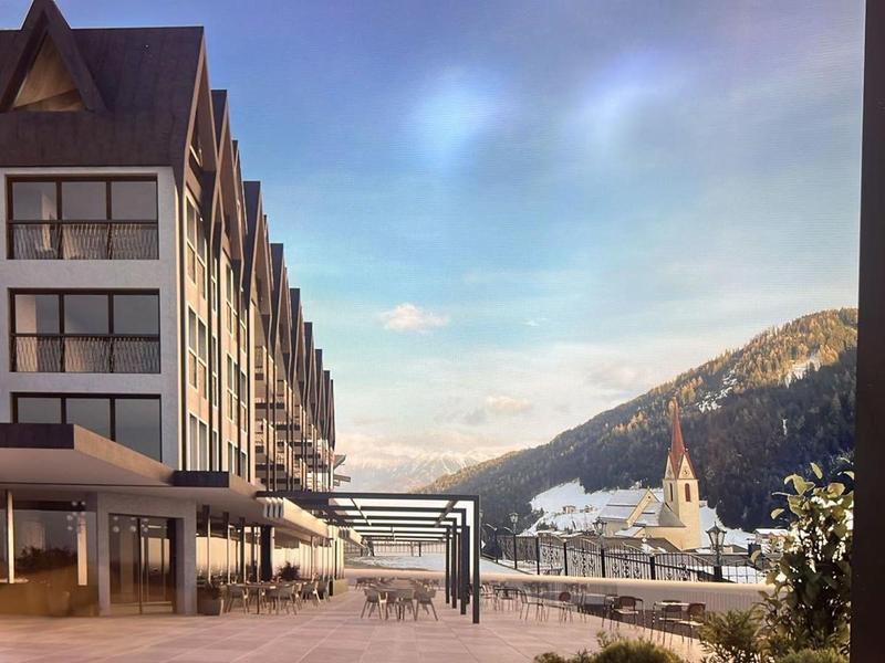 Modernes Hotelgebäude mit Bergblick und Kirche im Hintergrund bei Sonnenuntergang.