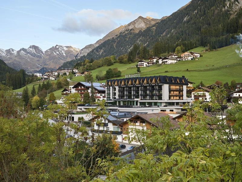 Hotel in einem grünen Tal mit Bergen im Hintergrund und bewaldeten Hügeln