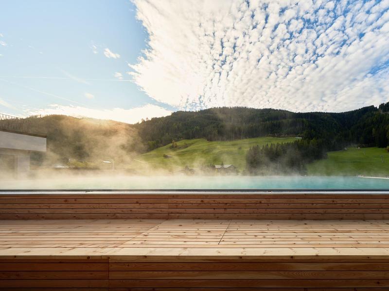 Dampf steigt von einem schwimmenden Pool vor einer hügeligen Landschaft bei Sonnenuntergang auf.