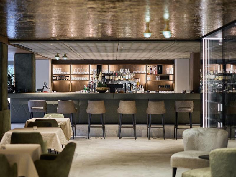 Moderner Hotelbarbereich mit Theke, Barhockern und Tischen in elegantem Ambiente.