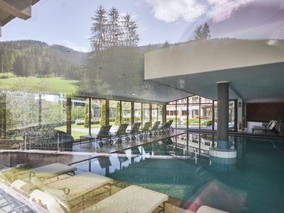 Innenpool mit Liegestühlen und großen Fenstern mit Blick auf eine bewaldete Landschaft.