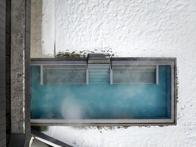 Rechteckiges Schwimmbecken mit blauem Wasser umgeben von schneebedecktem Boden und Betonrahmen.