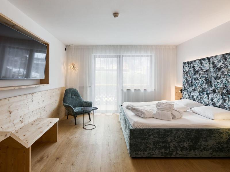 Gemütliches Schlafzimmer mit großem Fenster, dunkelblauem Bett und Holzfußboden.