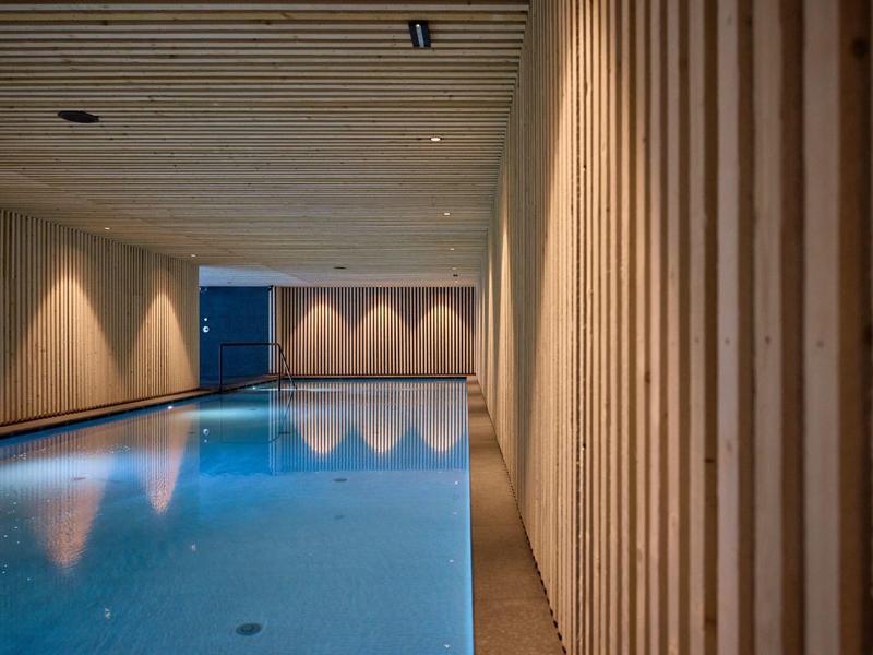 Moderner Innenpool mit blauen Wasser, Holzvertäfelungen an Wänden und Decke, weiche Beleuchtung.