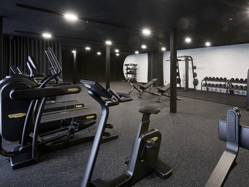 Dunkler Fitnessraum mit Cardio- und Kraftgeräten sowie schwarzen Teppichboden und Deckenlichtern.