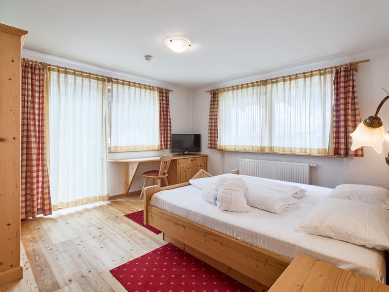 Helles Schlafzimmer mit Holzmöbeln, großem Bett, roten Teppichen und Gardinen vor großen Fenstern.