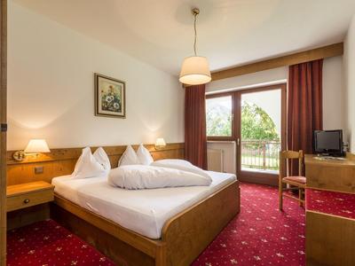 Gemütliches Schlafzimmer mit Doppelbett, roten Teppich, Holzmöbeln und Balkon mit Blick ins Grüne.