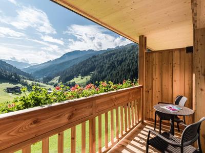 Balkon mit Tisch und Stühlen, Blick auf grüne Berge unter blauem Himmel.