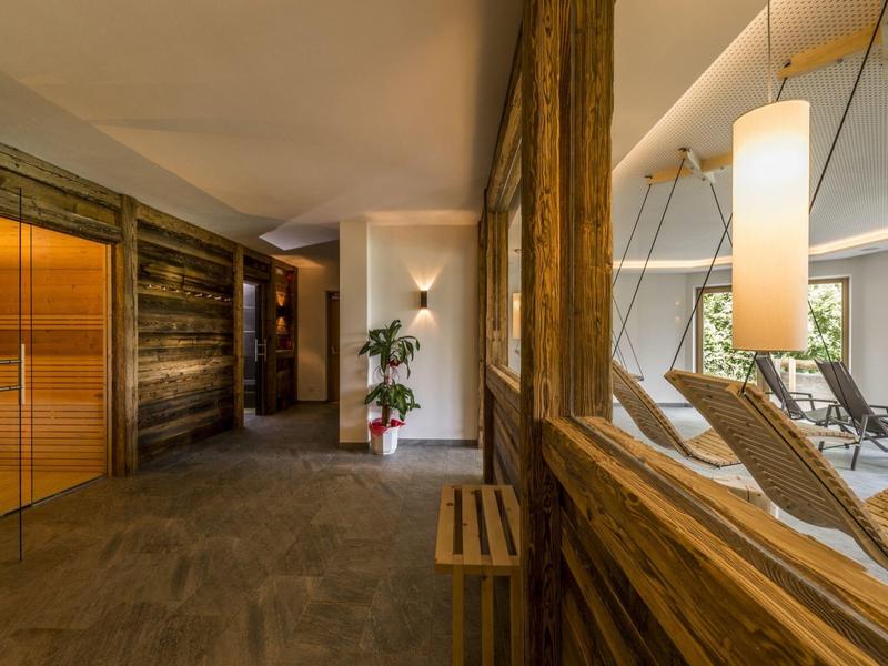 Moderner Wellnessbereich mit Holzwänden, Sauna, Pflanzen und Liegen an großen Fenstern.