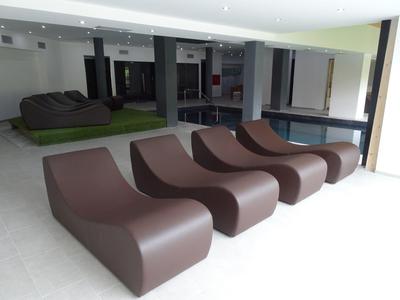 Moderne braune Loungesessel mit geschwungener Form stehen in einem hellen Raum mit großem Fenster.