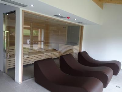 Moderner Saunaraum mit Glaswand und drei braunen Liegen in schlichtem, hellem Raum.