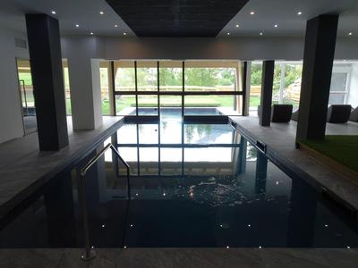 Innenraum mit rechteckigem Hallenbad, großen Fenstern und Blick auf Garten und Hausfassade.