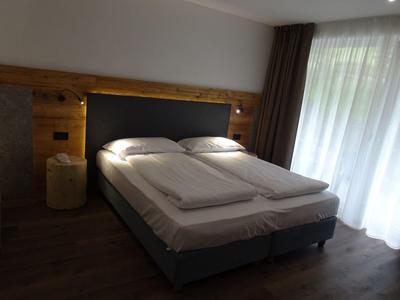 Modernes Schlafzimmer mit großem Doppelbett, Holzverkleidung und lichtdurchlässigen Vorhängen.