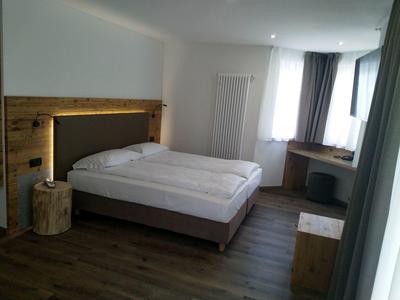 Schlichtes Schlafzimmer mit Doppelbett, Holzmöbeln, hellen Wänden und großem Fenster mit Vorhängen.