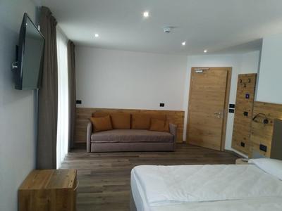 Modernes Hotelzimmer mit Doppelbett, braßfarbiger Couch, Holzmöbeln und weiß gestrichenen Wänden.