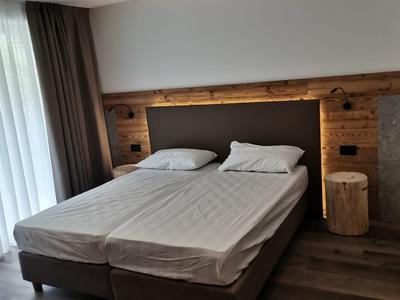 Modernes Schlafzimmer mit Doppelbett, Holzwand, Nachttisch aus Holzstamm und großen Fenstern.