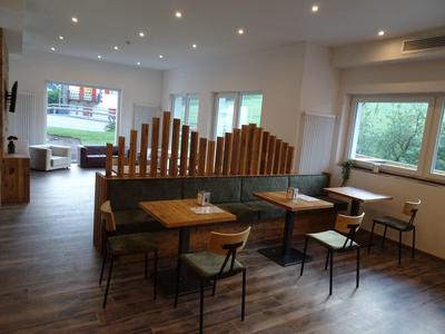 Modernes Café mit Holzboden, Tischen, Stühlen und großen Fenstern, viel natürlichem Licht.