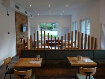 Moderner Gastraum mit Holzmöbeln, dunklem Boden und großen Fenstern zum Garten hin.