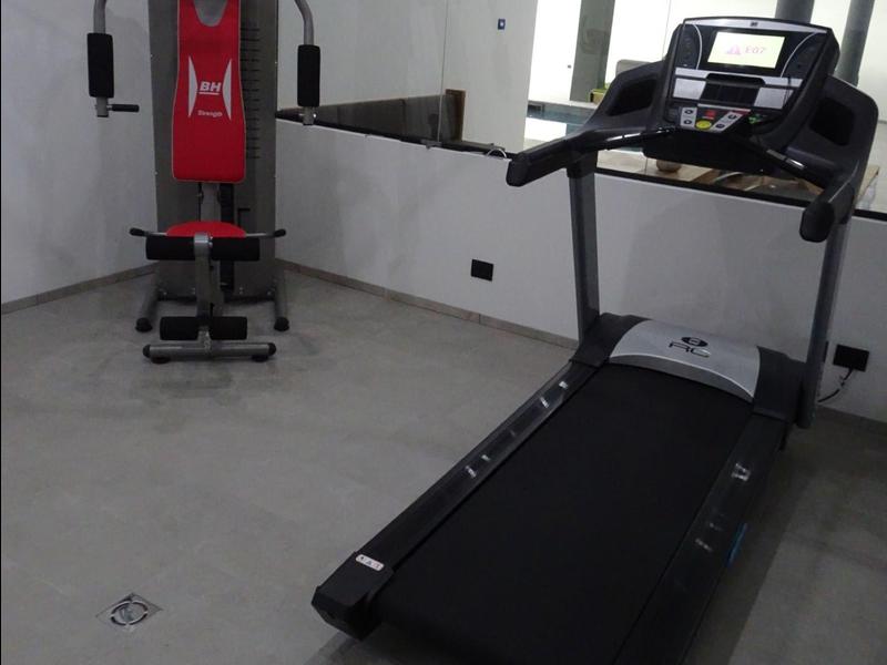 Ein Fitnessraum mit Laufband und Kraftstation vor weißen Wänden und grauem Boden.