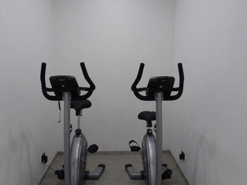 Zwei schwarze Fitnessfahrräder in einem kleinen, weißen Raum mit grauem Boden.