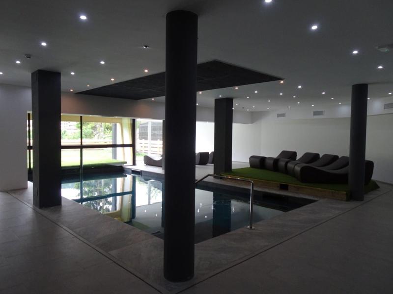 Moderner Innenpool mit schwarzen Säulen, weißen Wänden, Ledersofas und eingebauten Deckenlichtern.