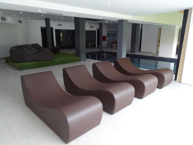 Moderne braune Loungesessel mit geschwungener Form stehen in einem hellen Raum mit großem Fenster.