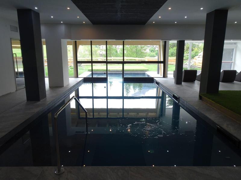 Innenraum mit rechteckigem Hallenbad, großen Fenstern und Blick auf Garten und Hausfassade.