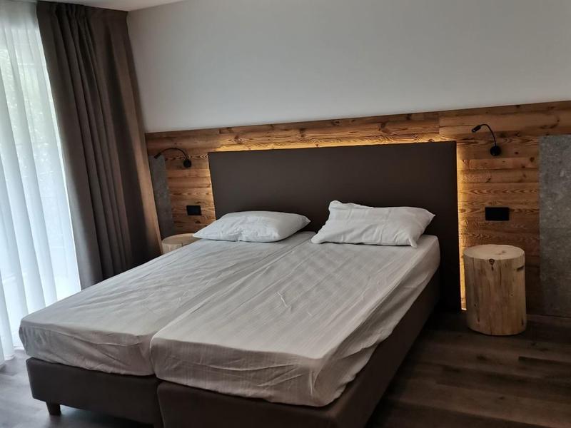 Modernes Schlafzimmer mit Doppelbett, Holzwand, Nachttisch aus Holzstamm und großen Fenstern.