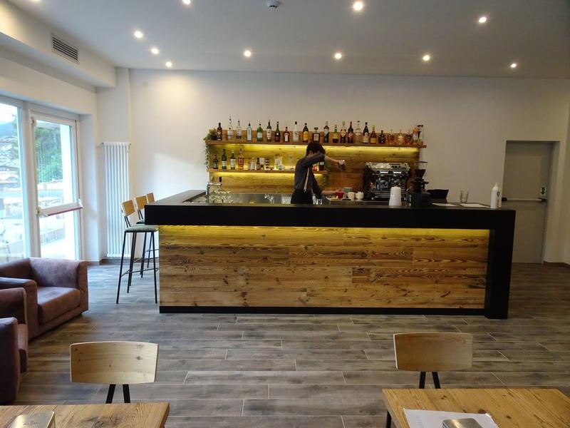 Moderner Cafébereich mit langem Holztheken, Barista und hellen Holzmöbeln.