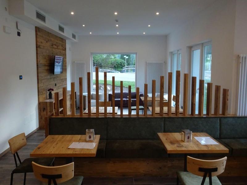 Moderner Gastraum mit Holzmöbeln, dunklem Boden und großen Fenstern zum Garten hin.