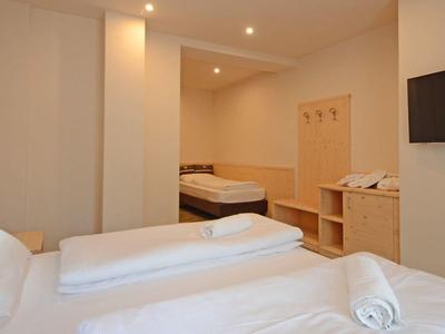 Einfaches Hotelzimmer mit Doppelbett, TV an der Wand und Holzmöbeln in heller Farbgebung.