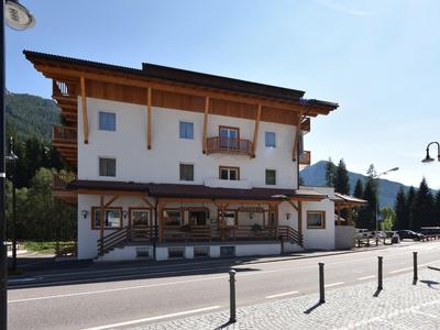 Dreistöckiges Gebäude mit Holzbalken, Balkon, Ladenfront und Bergkulisse im sonnigen Dorf.