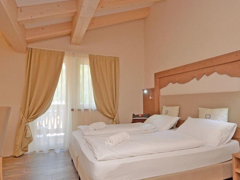 Helles Schlafzimmer mit weißem Bett, Holzmöbeln und großen Fenstern mit Vorhängen.