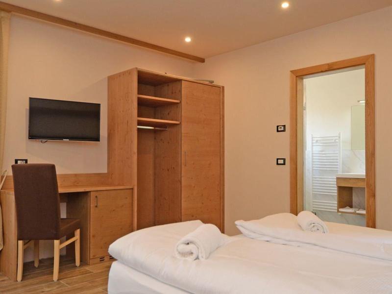 Helles Schlafzimmer mit Doppelbett, Holzmöbeln, Schreibtisch, Stuhl und Vorhängen am Fenster.