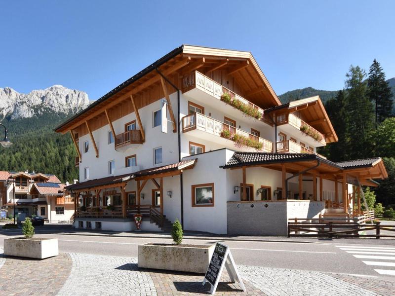 Großes, weißes Chalet mit Holzakzenten, umgeben von Bergen und blauem Himmel an einem sonnigen Tag.