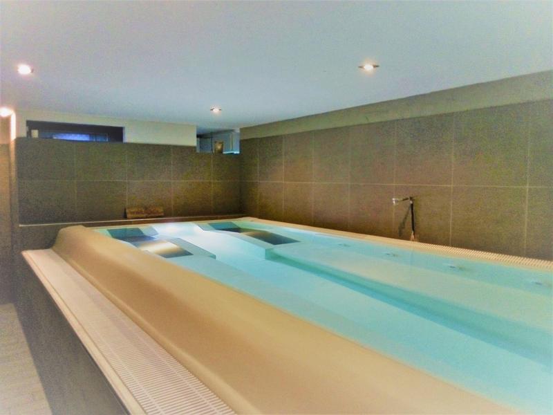 Modernes Hallenbad mit ruhigem Wasser, grauen Fliesen und dezenter Beleuchtung an der Decke.