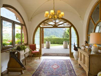 Ingresso luminoso con finestre ad arco, tappeto e vista sul giardino e le montagne.